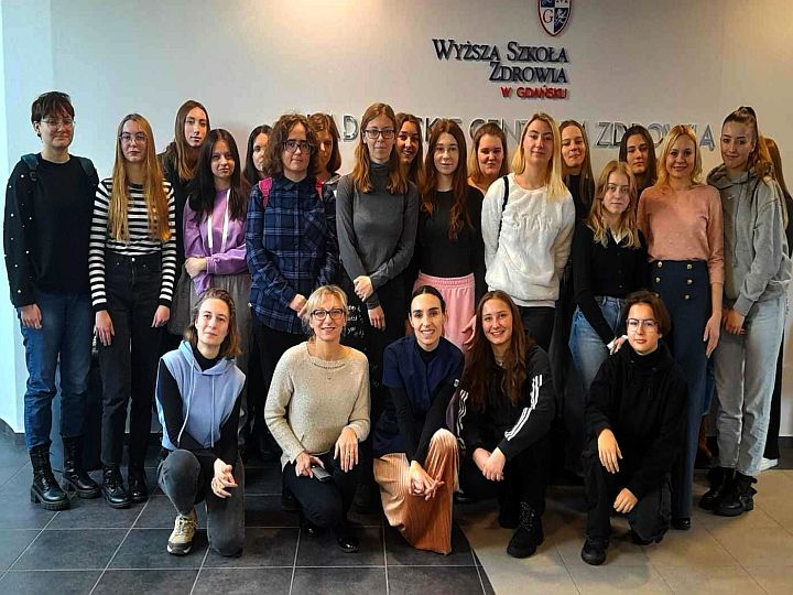 Grupa uczniów wraz z nauczycielami w tle na ścianie napis Wyższa Szkoła Zdrowia w Gdańsku