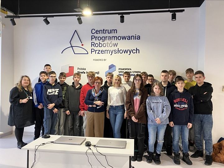 Grupa uczniów klasy pierwszej technik programista wraz z nauczycielem w tle na ścianie napis: centrum programowania robotów przemysłowych